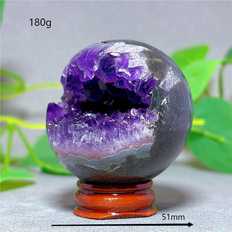 Amethyst geode crystal on a stand with green leaves in the background