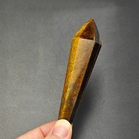 Tiger's eye crystal held by a hand against a gray background