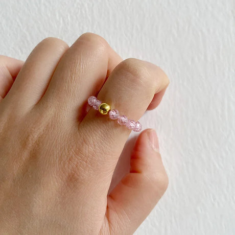 Hand wearing a pink beaded ring with a gold accent on a light background