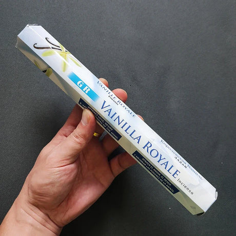 Hand holding a box of Vainilla Royale incense against a dark background