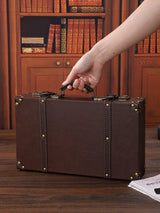 Brown leather suitcase being held by a hand in front of a bookshelf.
