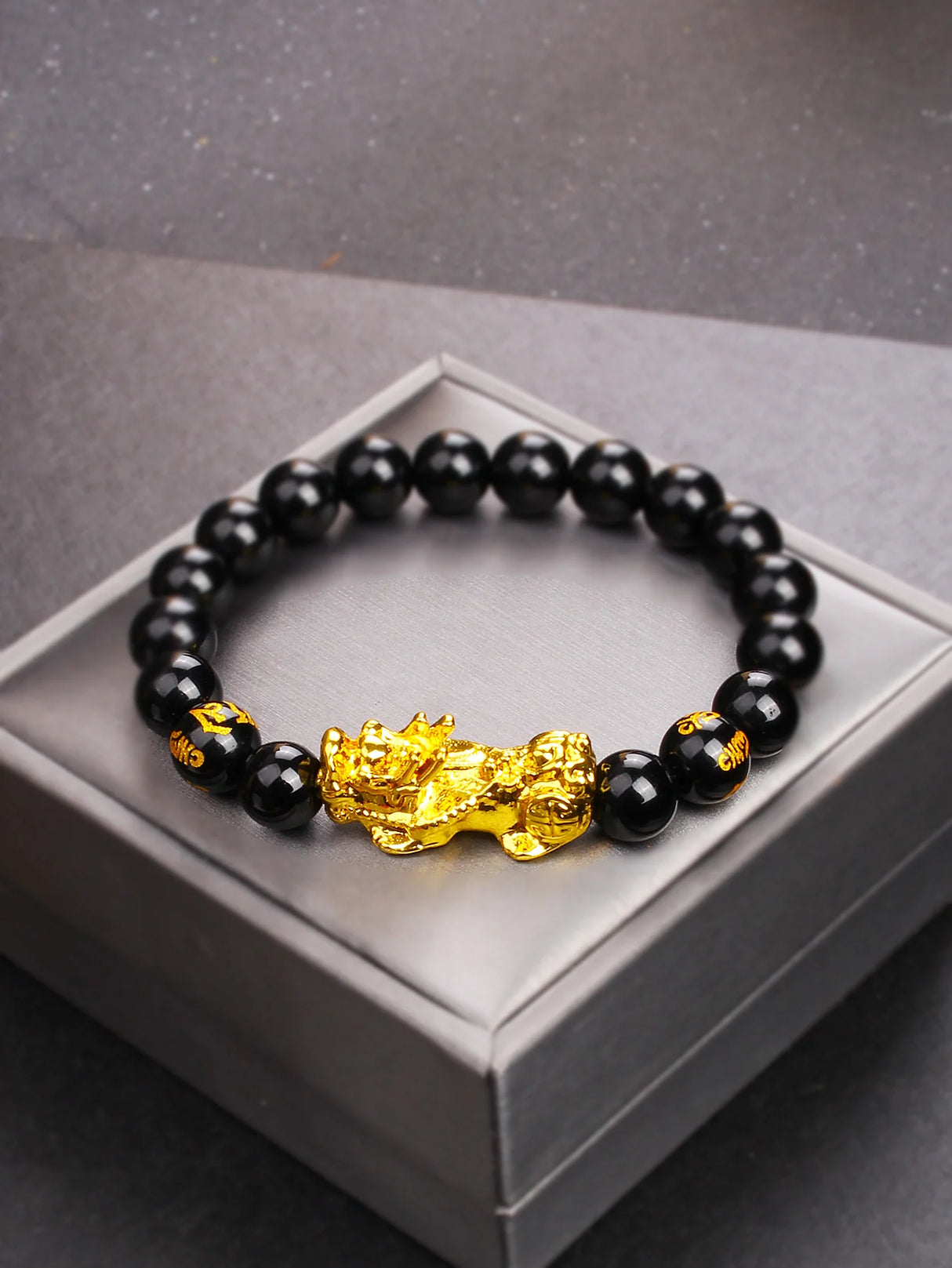 Black beaded bracelet with a gold dragon charm on a gray box