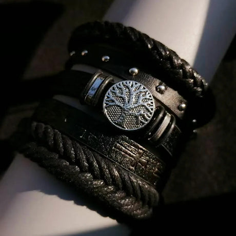 Close-up of a person wearing multiple dark leather bracelets with metallic accents on a light background