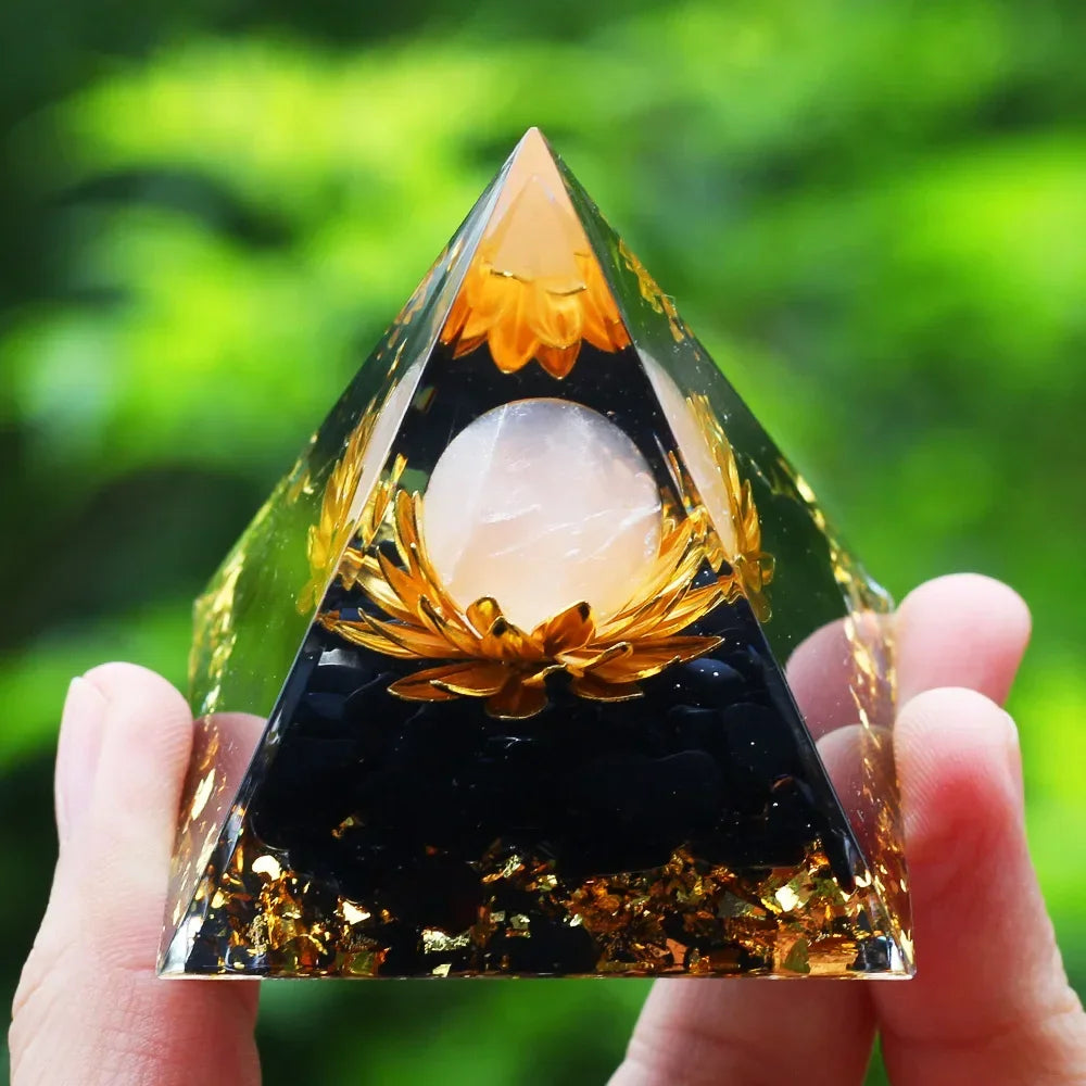 Pyramid-shaped crystal with a central sphere held by a hand against a blurred green background