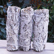 Three bundles of sage tied together with twine on a wooden surface with a natural background.