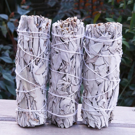 Three bundles of sage tied together with twine on a wooden surface with a natural background.