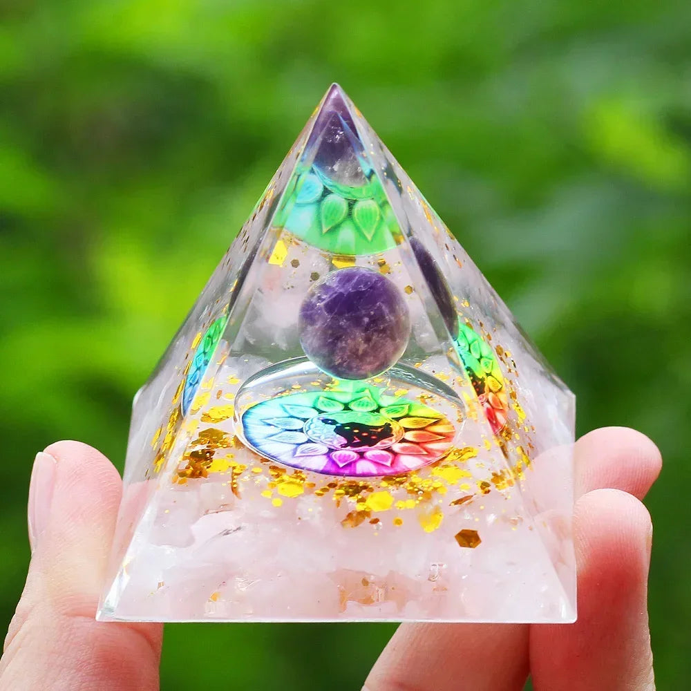 Pyramid-shaped crystal with colorful interior and amethyst stone held by a hand against a green blurred background