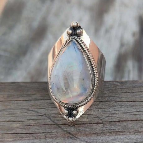Silver ring with a teardrop-shaped gemstone on a wooden surface
