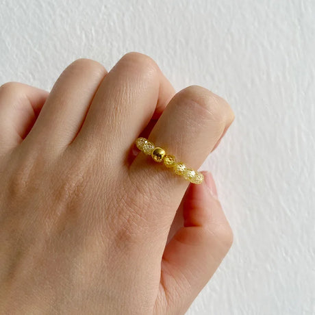 Gold beaded ring on a finger against a white background