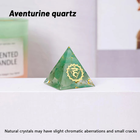 Green pyramid-shaped aventurine quartz crystal with a gold symbol on a white surface.
