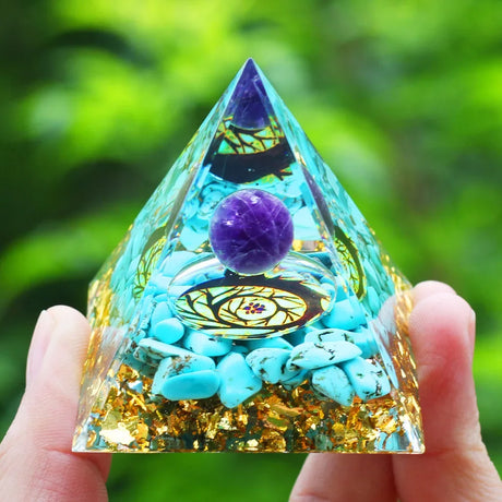 Pyramid-shaped crystal with purple ball and stones held by a hand against a green blurred background