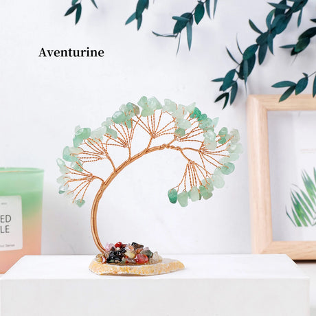 Decorative tree sculpture with aventurine stones on a white surface with greenery in the background.