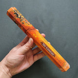 Hand holding a筒 of Sri Ganesh incense against a dark background