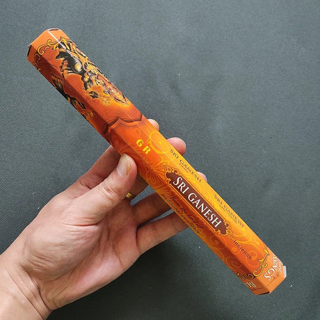 Hand holding a筒 of Sri Ganesh incense against a dark background