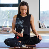 Woman in a black outfit sitting cross-legged with smoke in a room.