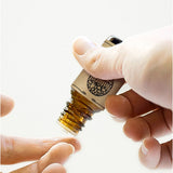 Hand holding a small brown bottle with a label against a white background
