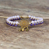 Bracelet with purple and white beads and a gold dreamcatcher charm on a wooden surface
