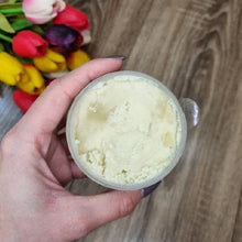 Dimollaure Organic Unrefined Shea Butter Oil container held by hand with flowers background.