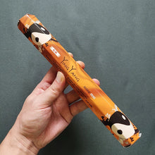 Hand holding a cylindrical incense box with cartoon character design against a gray background