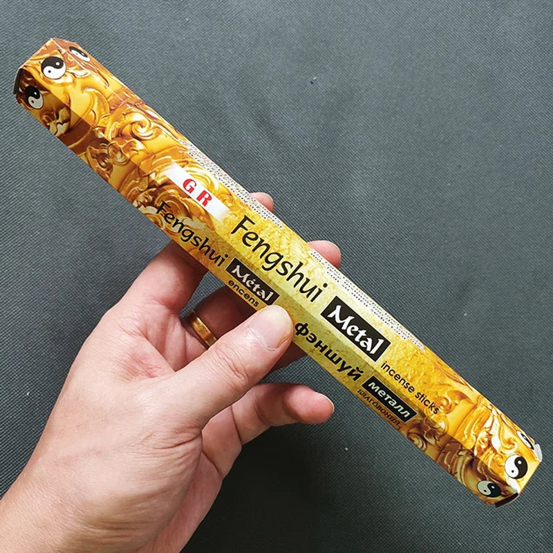 Hand holding a package of Fengshui Metal incense sticks against a dark background