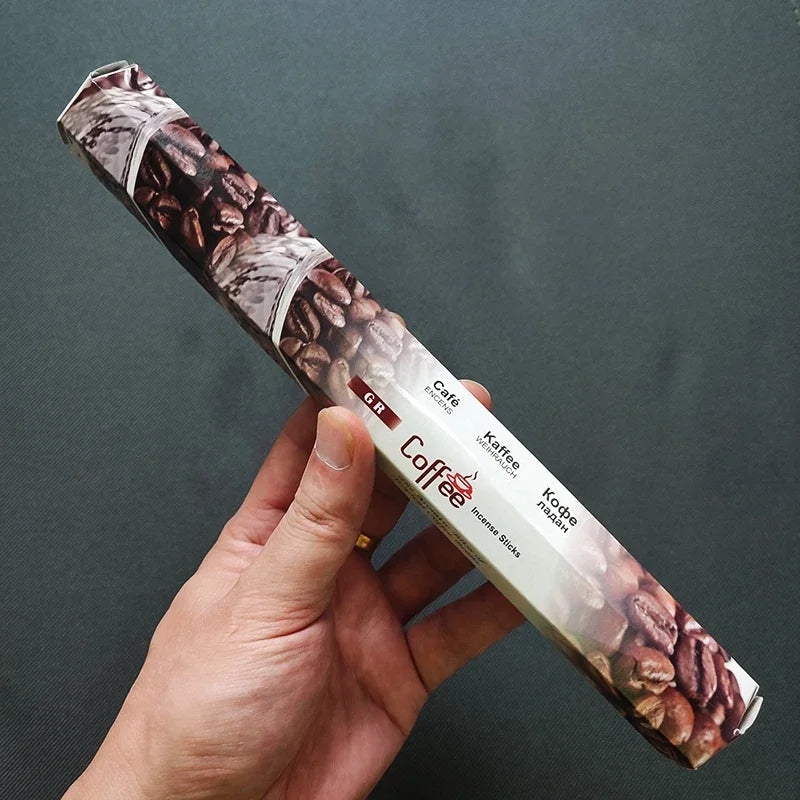 Hand holding a package of coffee incense sticks with a dark background