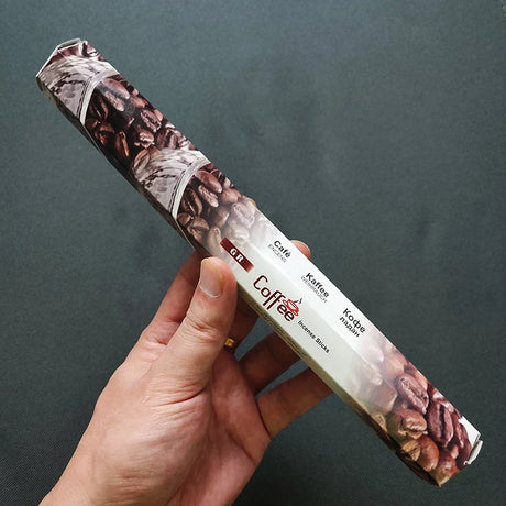 Hand holding a package of coffee incense sticks with a dark background