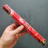 Hand holding a red Cherry incense packaging against a gray background