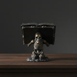 Skeleton holding spell book figurine close-up detail of sculpted design.