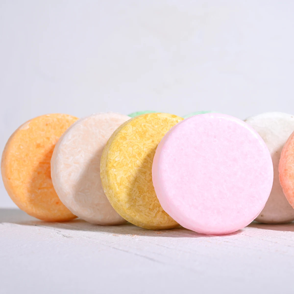 Row of colorful solid shampoo soap bars including Tea Tree Essential Oil variety on light background.