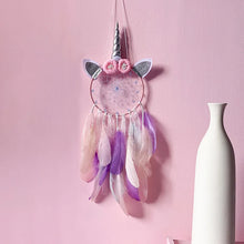 Unicorn-themed dreamcatcher with feathers on a pink wall next to a white vase.