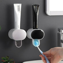 Automatic Toothpaste Dispenser wall-mounted with toothbrush holder on bathroom tile surface.